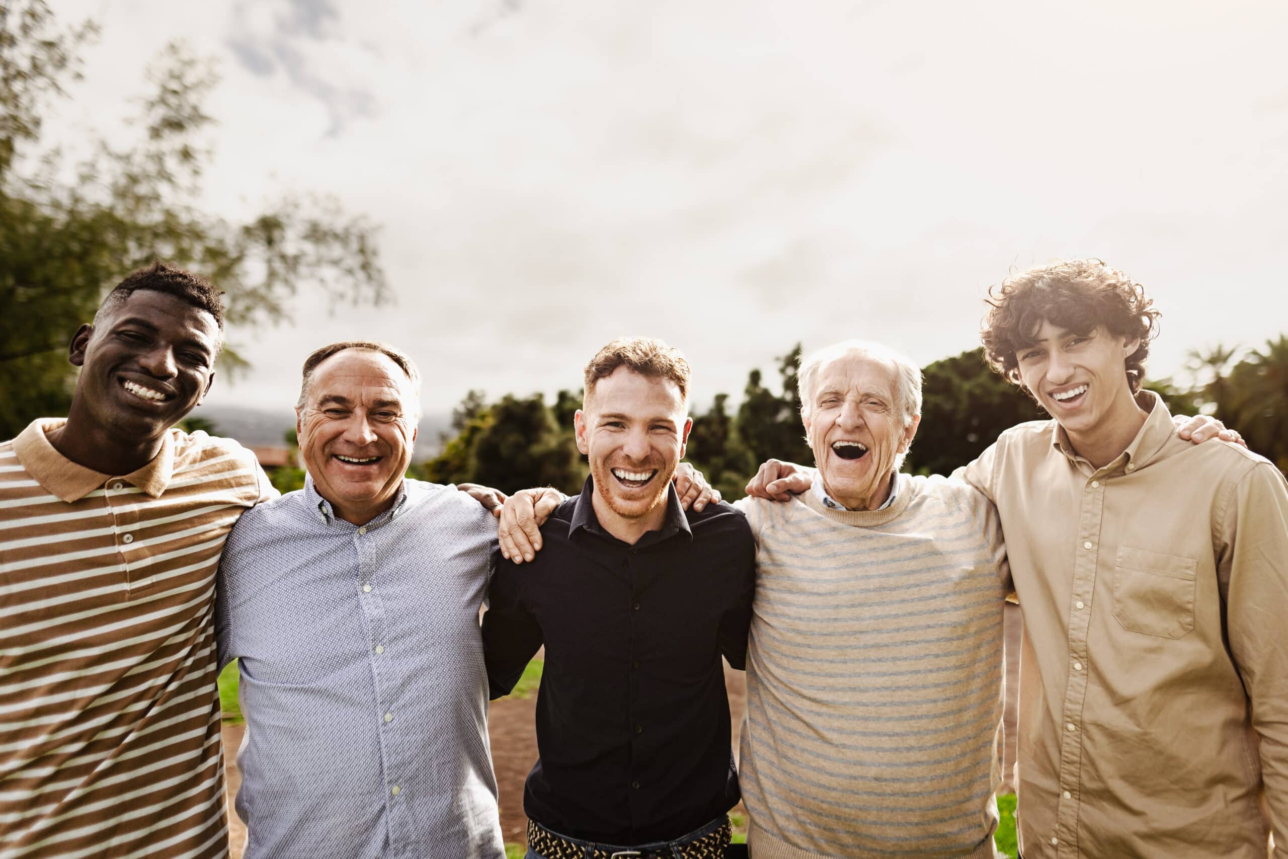 Happy multigenerational group of men with different ages and ethnicities having fun smiling in front of camera at park