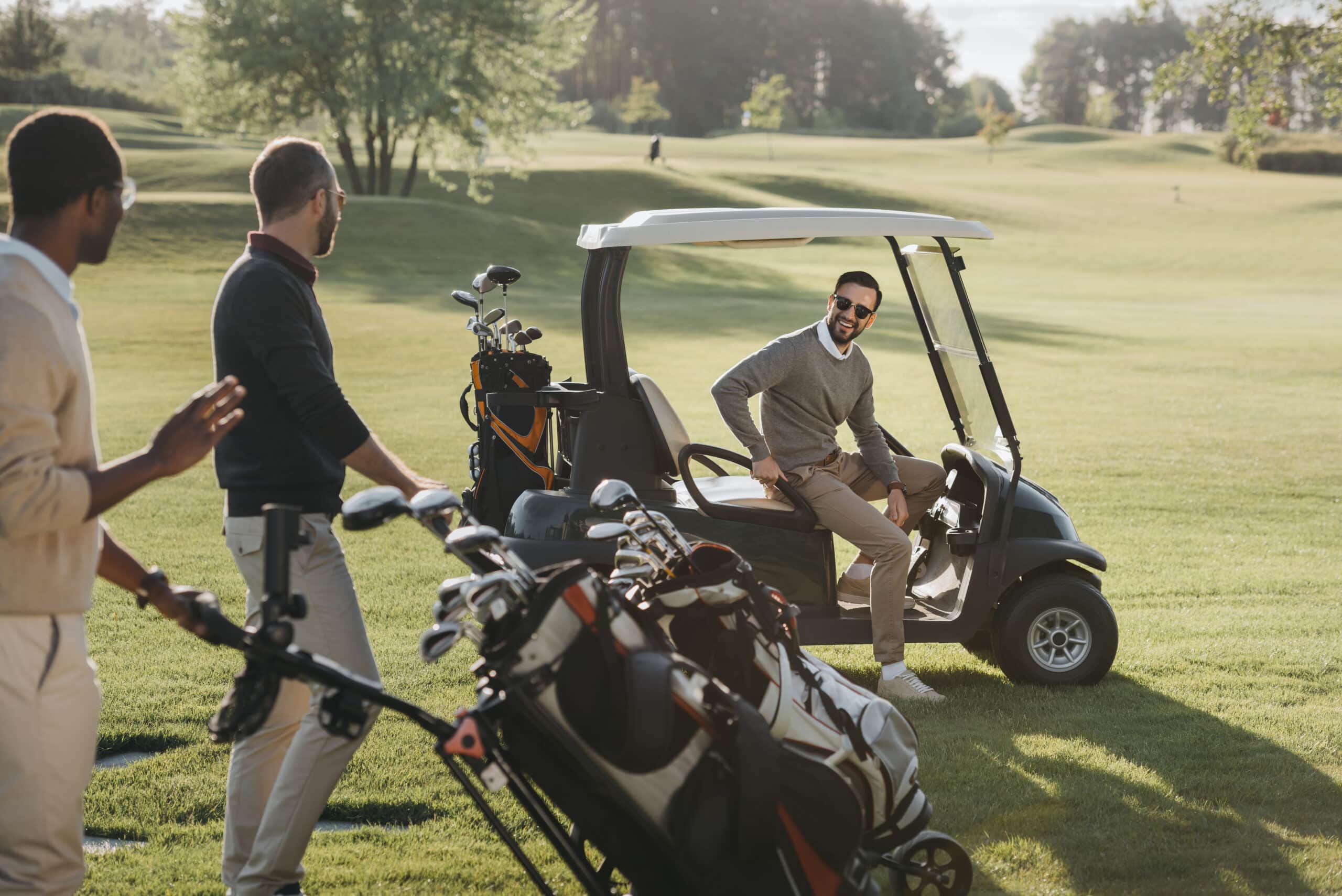multiethnic friends with golf bags and golf cart spending time together on golf course