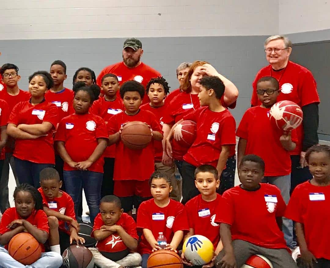 Children in red shirts holding basketballs with Men Serving God volunteers at a youth sports outreach event
