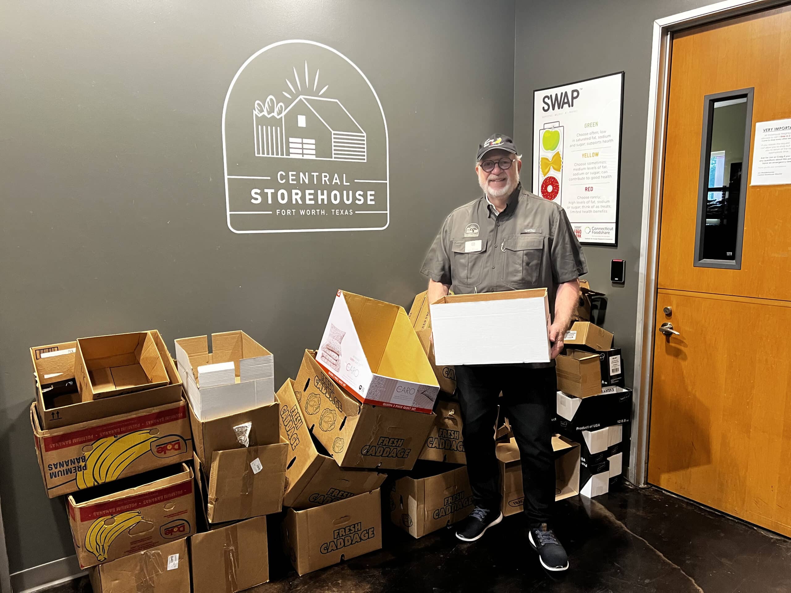 Ed Frazier holding a box at the Central Storehouse in Fort Worth, Texas, surrounded by empty cardboard boxes for Men Serving God food ministry