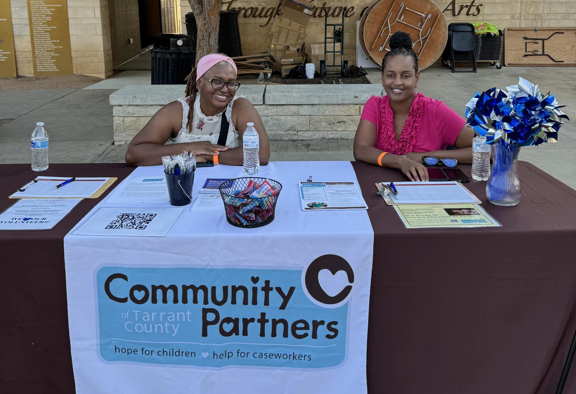 Community Partners Booth at Men Serving God Event - Men Serving God Two women at the Community Partners of Tarrant County table sharing resources for children and caseworkers at a Men Serving God community event