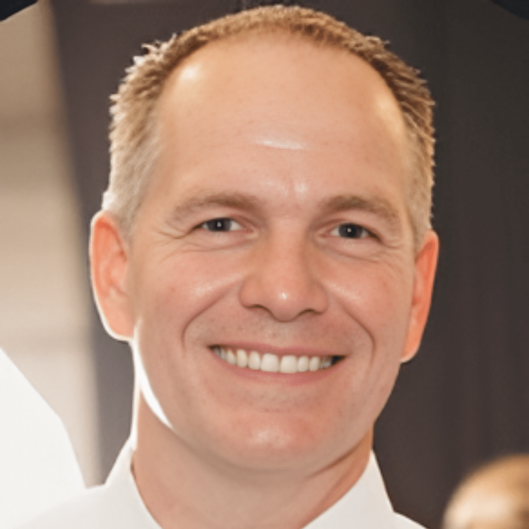Smiling man with short light brown hair in a white shirt, close-up portrait.